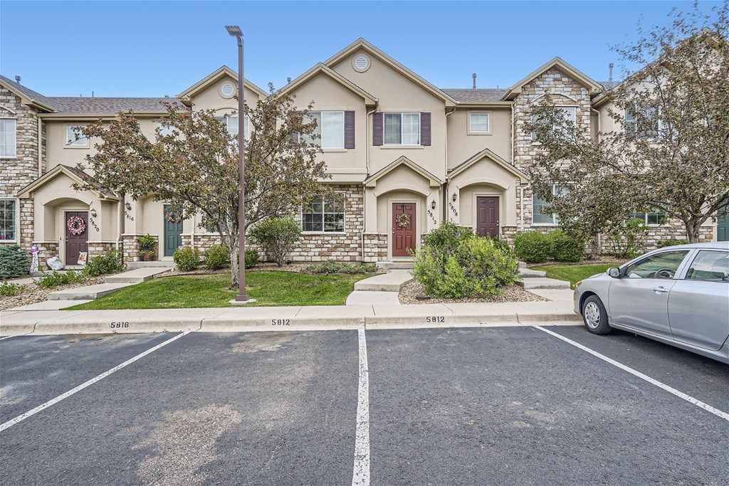 A silver car is parked in a parking lot in front of a two-story house.