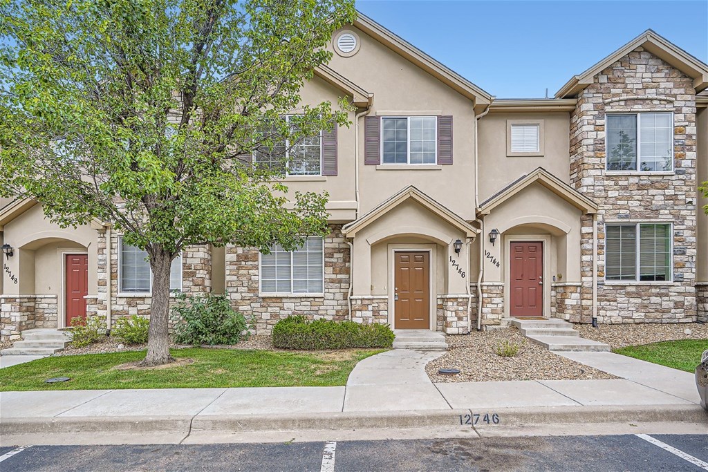 A two-story house with a red door and a tree in front.