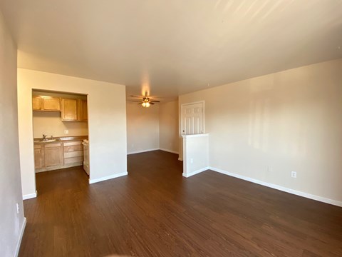 A room with wooden floors and a kitchen area in the background.