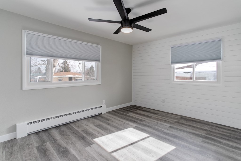 an empty living room with a ceiling fan and two windows