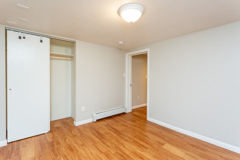 a bedroom with white walls and wood flooring and a closet