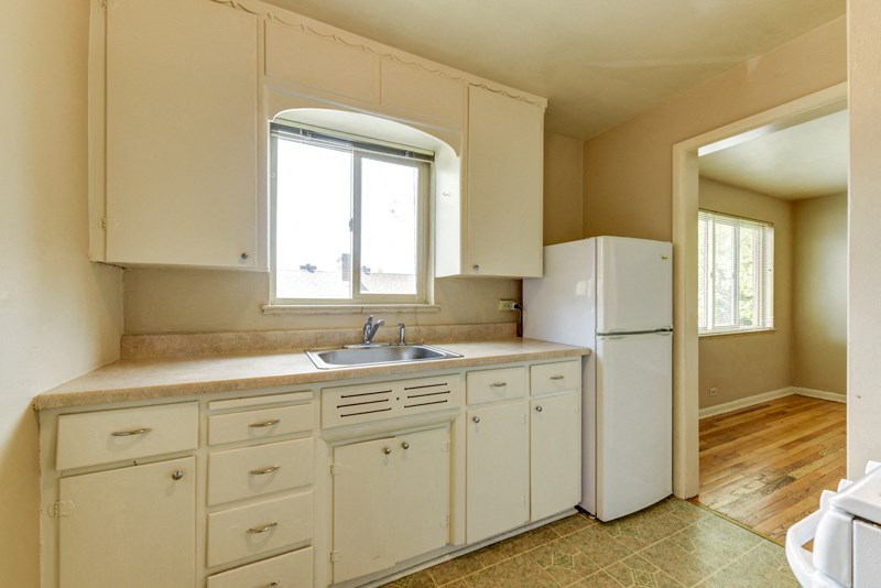 an empty kitchen with white cabinets and a window