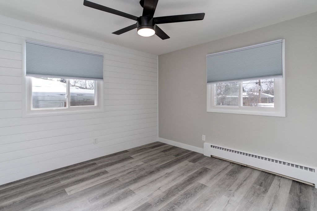 an empty bedroom with a ceiling fan and two windows