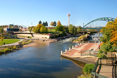 A river flows through a city with a bridge and a lighthouse in the background.