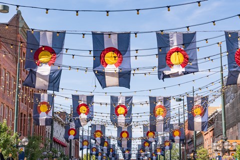 A series of flags with a sun design are strung between two buildings.