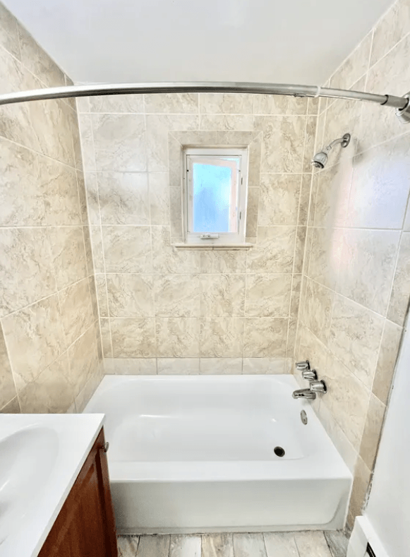 A white bathtub with a shower head and a window in the wall.
