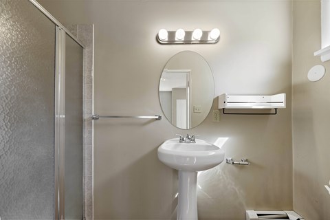 A white pedestal sink with a mirror above it and a towel rack to the right.