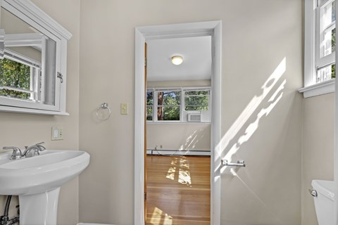 A white bathroom with a sink, mirror, and a door leading to a balcony.