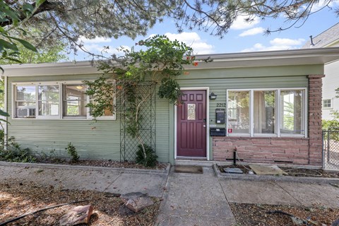 A green house with a red door and a mailbox with the number 2212 on it.