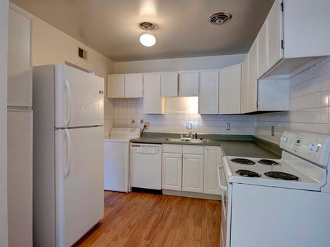 A white kitchen with a refrigerator, dishwasher, and stove.