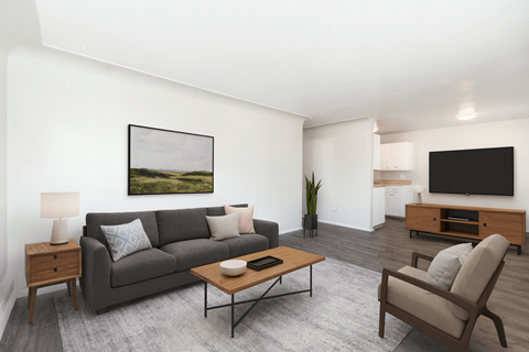 A living room with a grey couch, a wooden coffee table, a lamp, a painting, a television, and a plant.