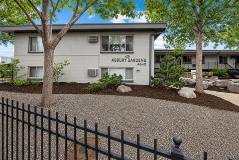 A black fence in front of a white building with the words ASBURY GARDENS on it.