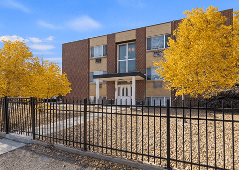 A brick building with a black fence and yellow trees in front.