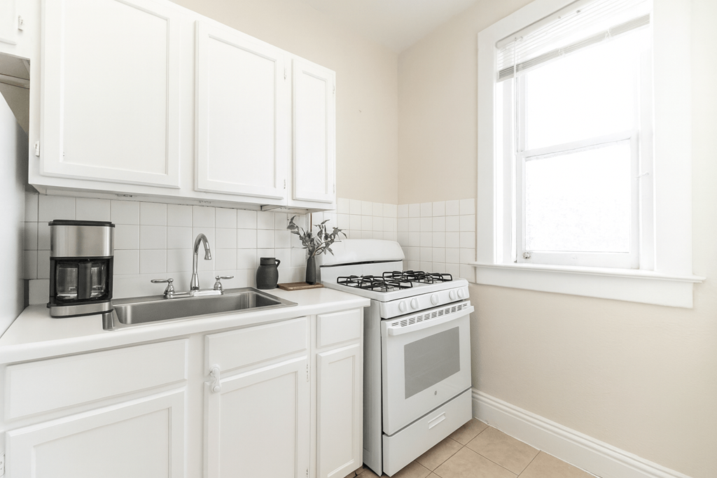 A white kitchen with a stove, sink, and cabinets.