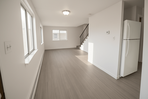 A white refrigerator sits in a room with a staircase.