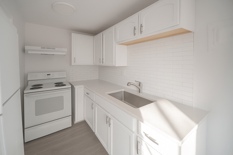 A white kitchen with a stove, sink, and cabinets.