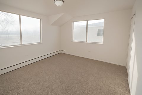 A room with carpeted floor and three windows.