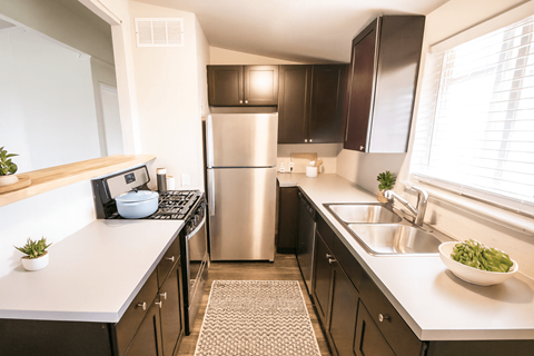 A modern kitchen with a stainless steel refrigerator and a sink with a bowl of green vegetables on the counter.