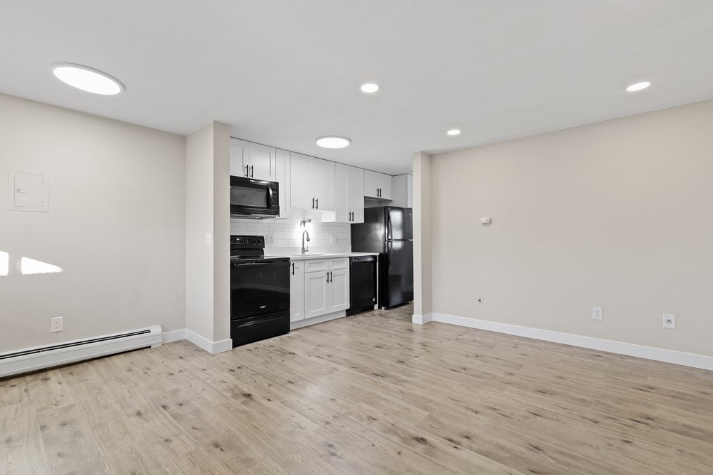 an empty room with white walls and a kitchen with black appliances