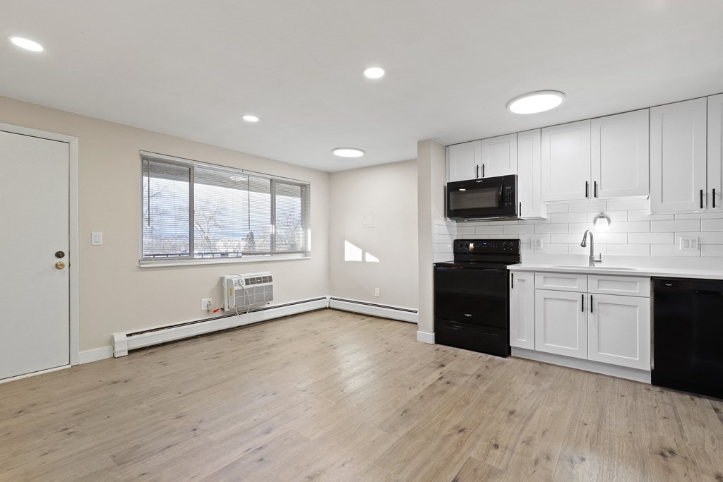 an empty kitchen and living room with white cabinets and black appliances