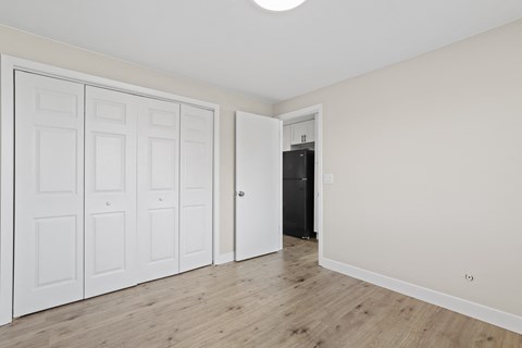 a bedroom with white walls and wood floors and a closet