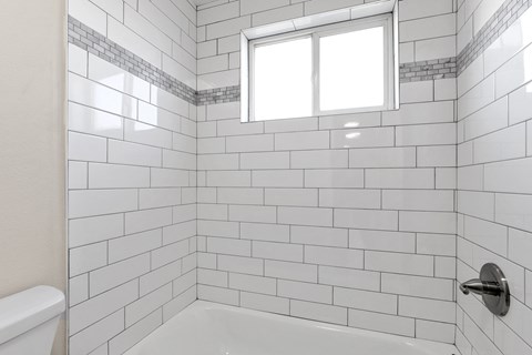 a white tiled bathroom with a window and a tub