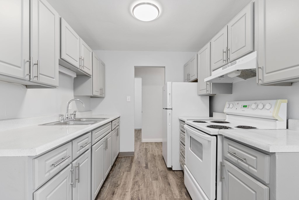 A white kitchen with a refrigerator, stove, and sink.