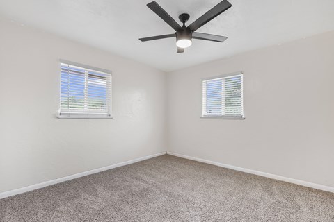 A room with a ceiling fan and two windows.
