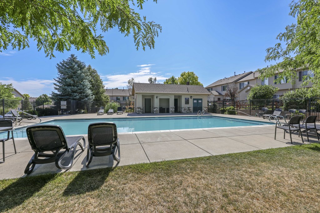Two lounge chairs sit on the lawn in front of a pool and a house.