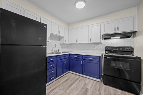 A black refrigerator is on the left in a kitchen with blue cabinets.