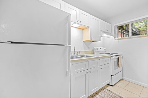 A white kitchen with a refrigerator, sink, and oven.