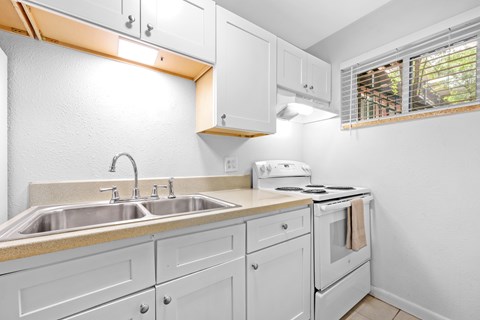 A white kitchen with a stove, sink, and cabinets.