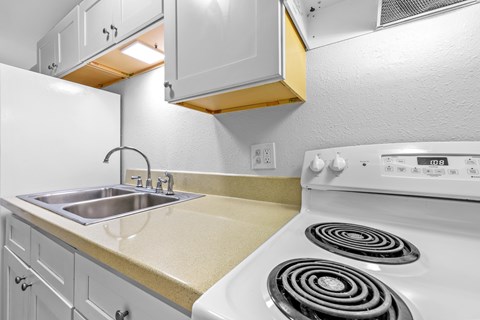A white stove with two burners is in a kitchen with white cabinets.