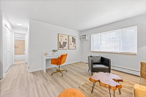A living room with a white desk, a black chair, and a wooden coffee table.