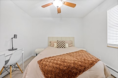 A bedroom with a bed, chair, and ceiling fan.