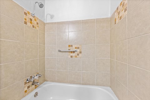A white bathtub with a shower head and a tiled wall.