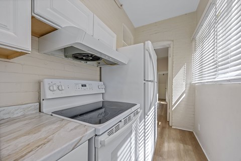 A white kitchen with a stove top oven and a refrigerator.