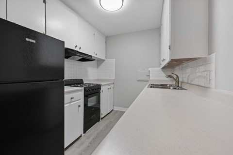 A black refrigerator is on the left in a white kitchen.