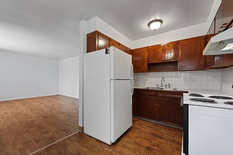 A white refrigerator stands in a kitchen with brown cabinets and a white stove.