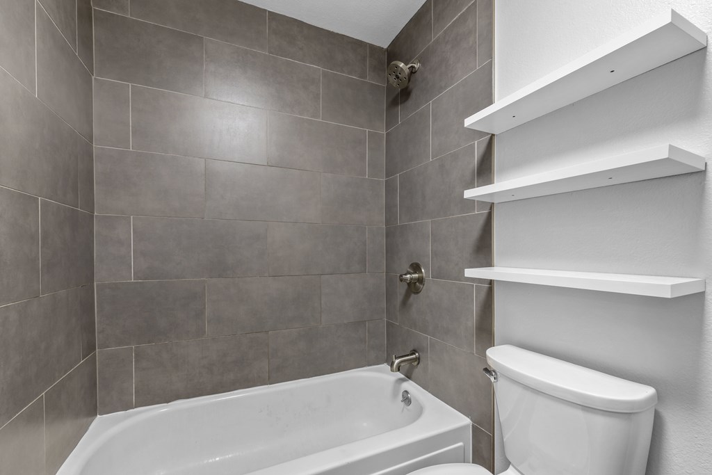 A white bathtub sits next to a toilet in a tiled bathroom.