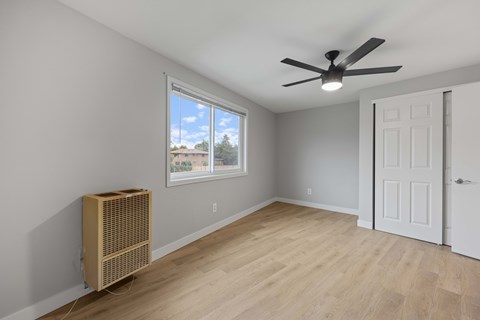 A room with a ceiling fan and a window with a view of a building and trees outside.