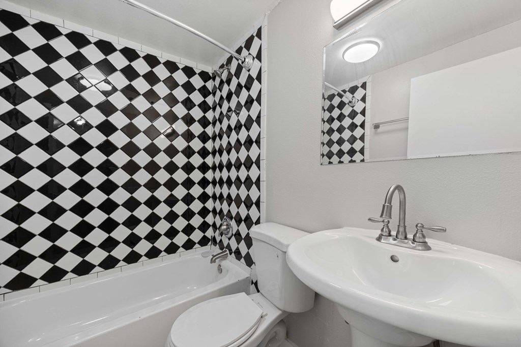 A black and white checkered bathroom with a toilet, sink and bathtub.