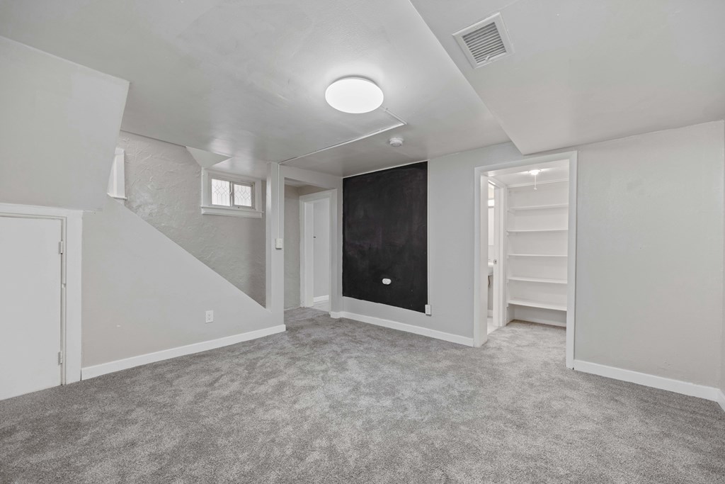 A spacious room with a staircase on the left and a blackboard on the right.