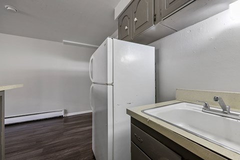 A white refrigerator stands in a kitchen next to a sink.