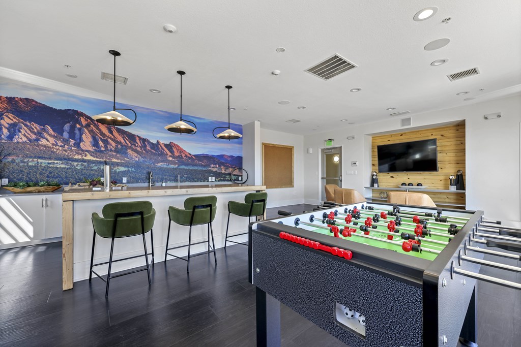 A foosball table is in the middle of a room with a bar and chairs.