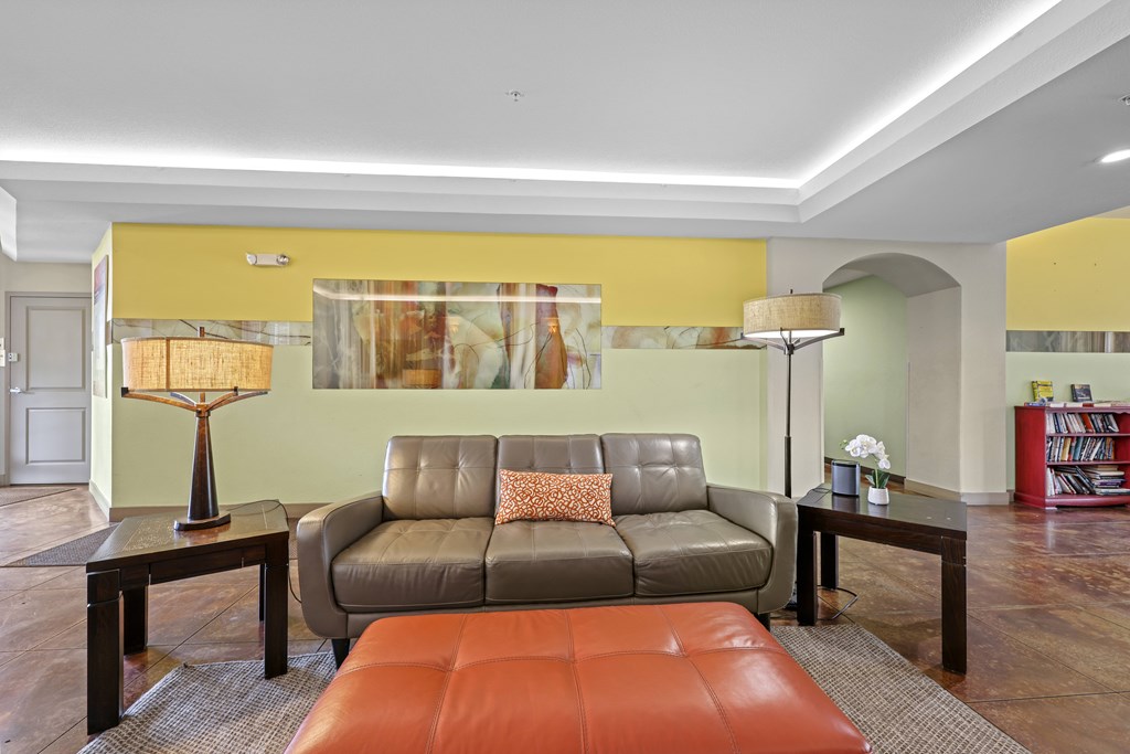 A living room with a grey couch, a brown ottoman, and a yellow accent wall.