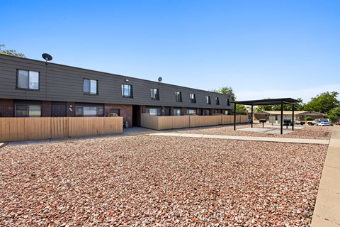 A building with a grey facade and a brown roof is surrounded by a gravel area.