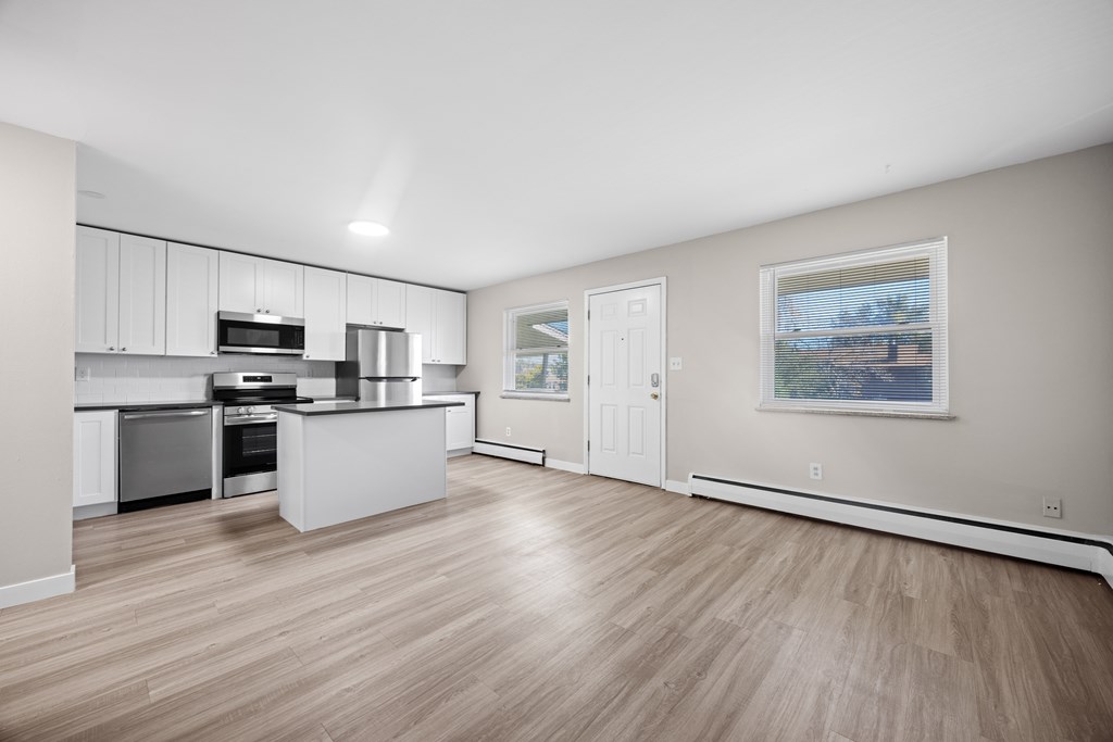 A spacious kitchen with light wood flooring and white cabinetry.