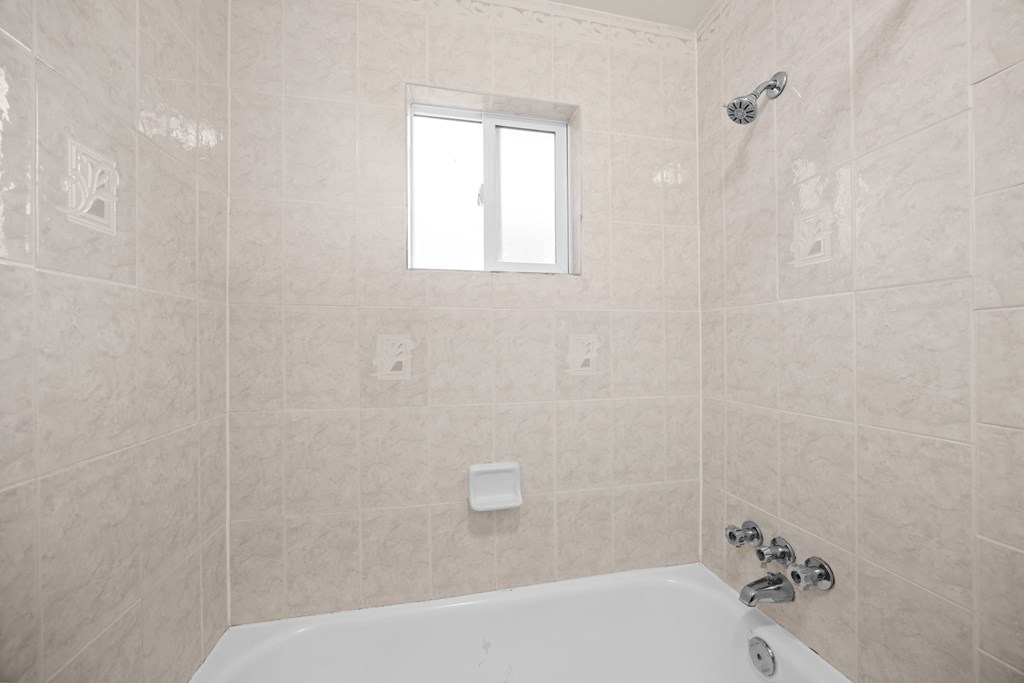 A white bathtub in a bathroom with a window above it.