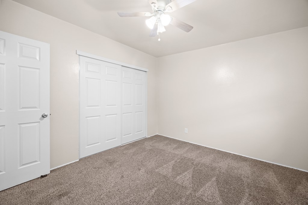A room with a carpeted floor and a ceiling fan.